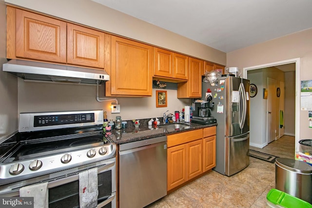 kitchen featuring appliances with stainless steel finishes, under cabinet range hood, a sink, and dark stone countertops