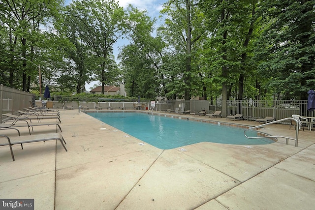 community pool featuring a patio area, fence, and view of scattered trees