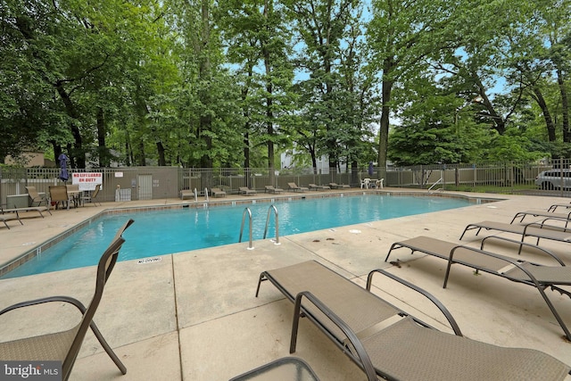 community pool with a patio area, fence, and view of scattered trees