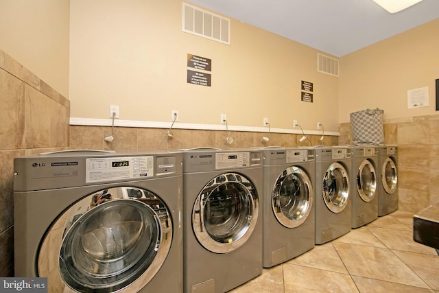 shared laundry room with tile walls, washing machine and dryer, light tile patterned floors, and a wainscoted wall