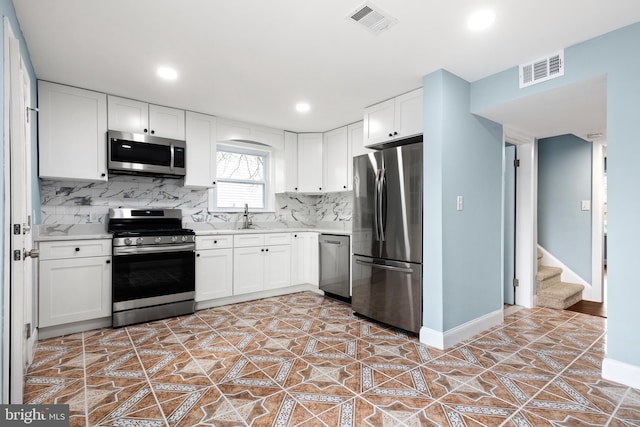 kitchen featuring appliances with stainless steel finishes, light countertops, decorative backsplash, white cabinetry, and baseboards