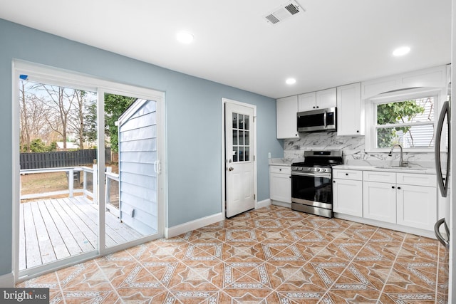 kitchen with appliances with stainless steel finishes, a sink, decorative backsplash, white cabinetry, and baseboards