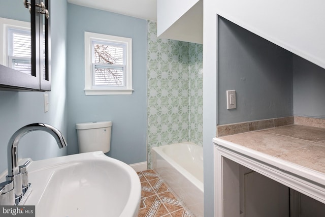 bathroom with a sink, healthy amount of natural light, tile patterned floors, wallpapered walls, and toilet