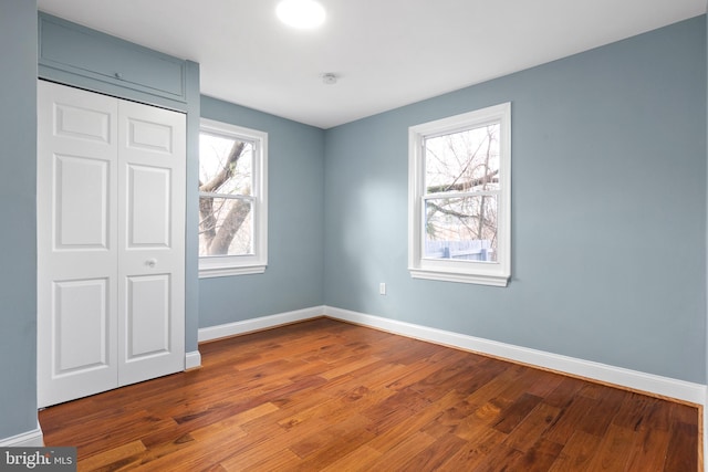 unfurnished bedroom with wood finished floors, baseboards, and a closet