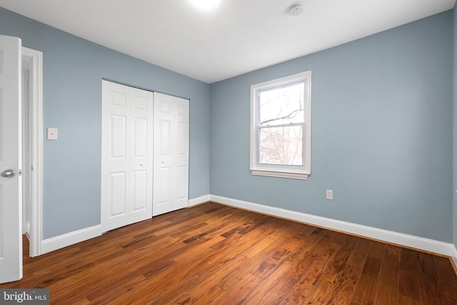 unfurnished bedroom featuring baseboards, dark wood finished floors, and a closet
