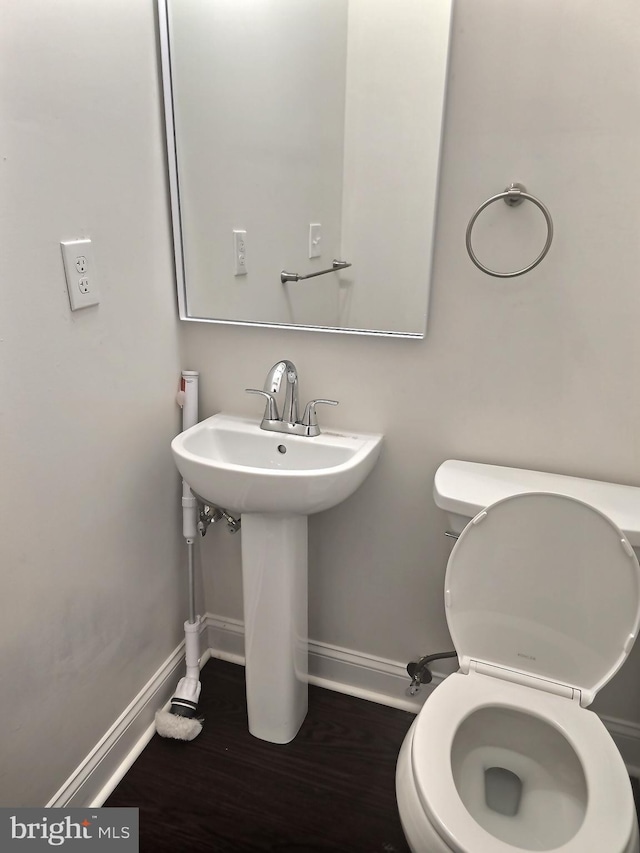 half bath with baseboards, toilet, a sink, and wood finished floors