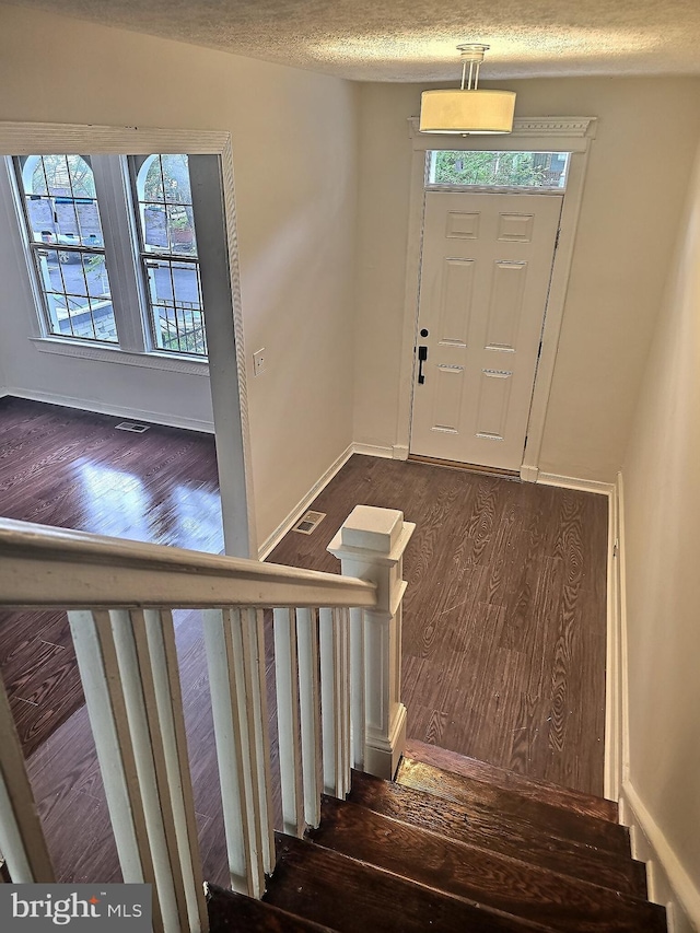 foyer entrance featuring wood finished floors, healthy amount of natural light, stairs, and a textured ceiling