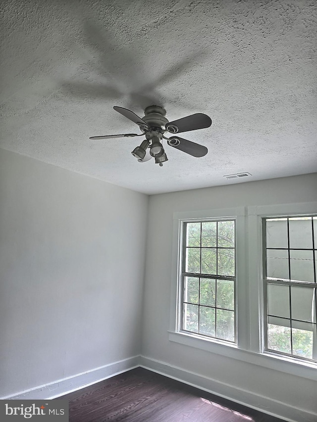 unfurnished room featuring a textured ceiling, dark wood-style flooring, plenty of natural light, baseboards, and ceiling fan