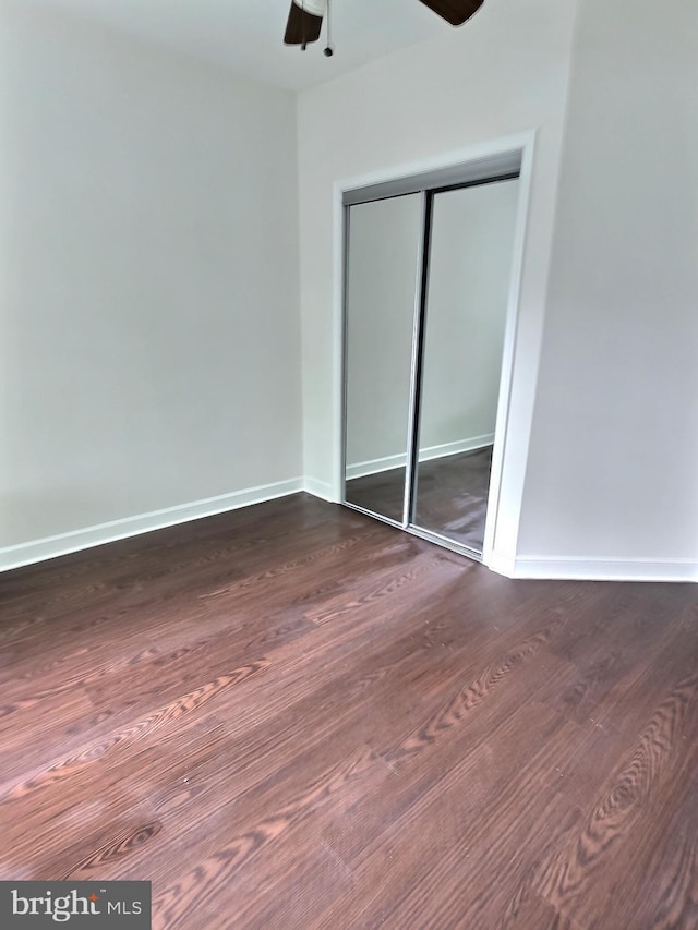 unfurnished bedroom with dark wood finished floors, a closet, baseboards, and ceiling fan