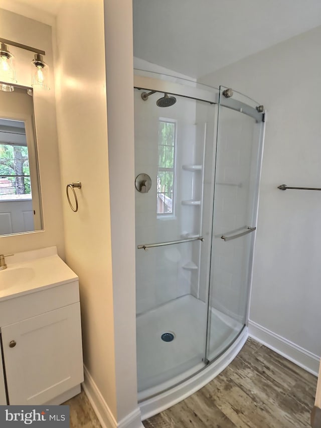 bathroom featuring wood finished floors, a shower stall, baseboards, and vanity