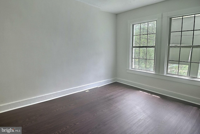spare room with healthy amount of natural light, baseboards, and dark wood-style floors