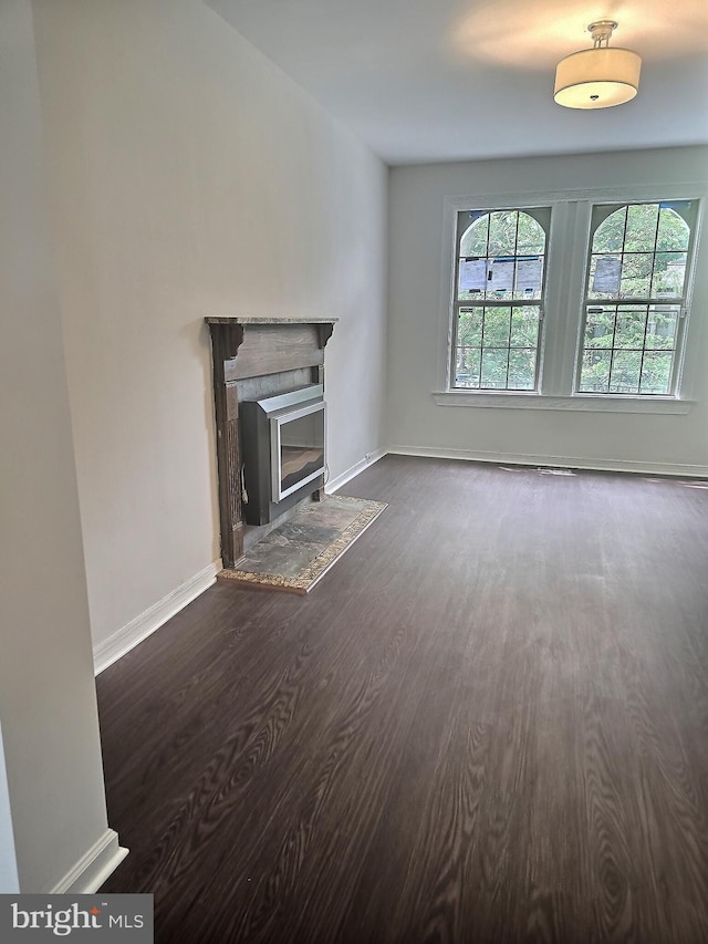 unfurnished living room featuring dark wood-style flooring, a fireplace with flush hearth, and baseboards