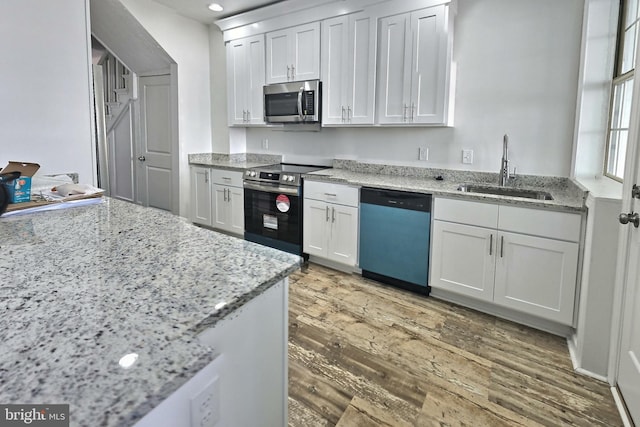 kitchen with stainless steel appliances, a sink, wood finished floors, white cabinets, and light stone countertops