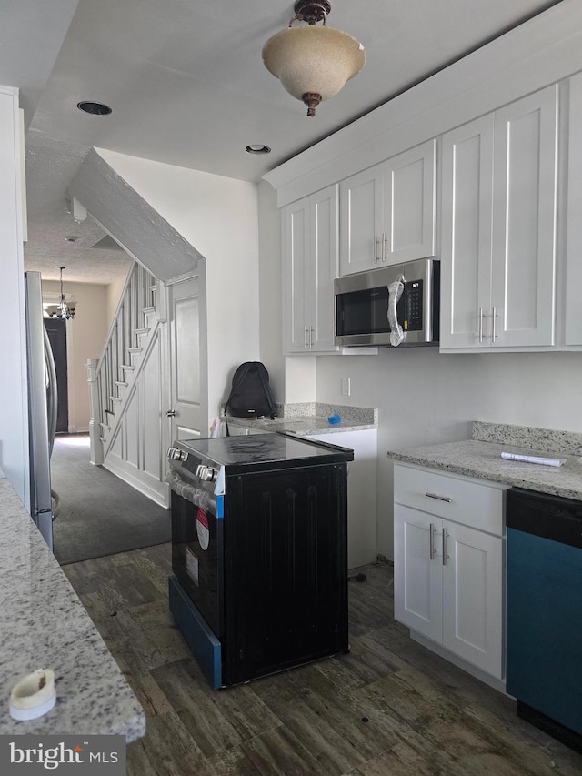 kitchen with appliances with stainless steel finishes, dark wood finished floors, white cabinets, light stone counters, and a chandelier