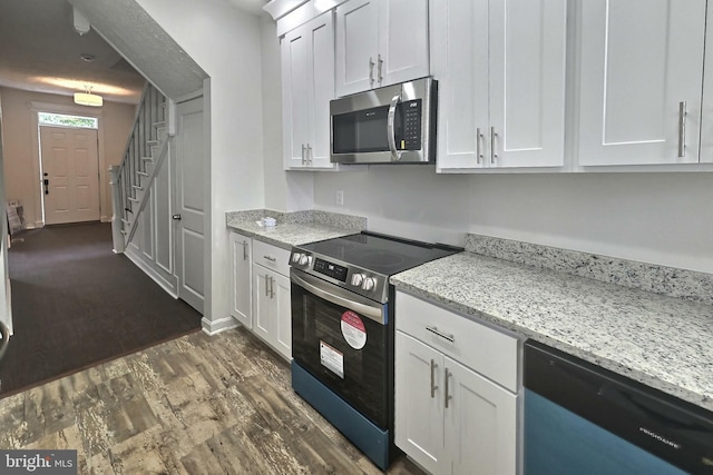 kitchen with appliances with stainless steel finishes, white cabinetry, dark wood-style flooring, and light stone countertops