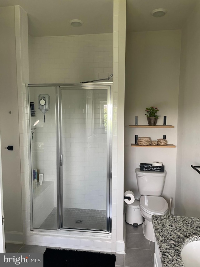 bathroom featuring tile patterned flooring, a stall shower, vanity, toilet, and baseboards
