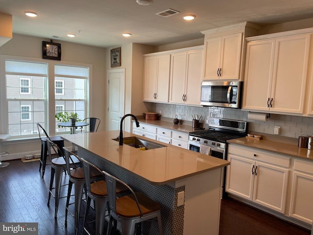 kitchen featuring appliances with stainless steel finishes, a sink, tasteful backsplash, white cabinets, and an island with sink