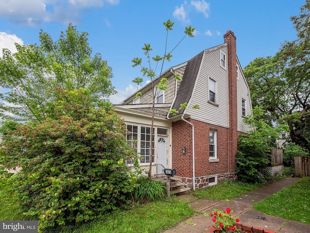 colonial inspired home featuring brick siding, a chimney, fence, and a gambrel roof