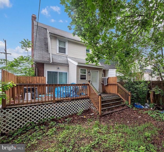 rear view of house featuring a chimney, a deck, and fence