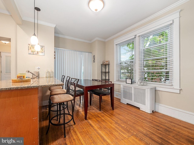 dining space featuring radiator heating unit, wood finished floors, crown molding, and baseboards