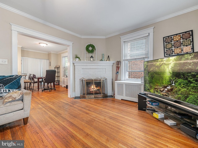 living room featuring radiator, wood-type flooring, crown molding, and a brick fireplace