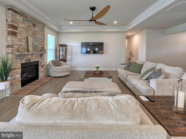 living room featuring a ceiling fan, wood finished floors, ornamental molding, a stone fireplace, and baseboards