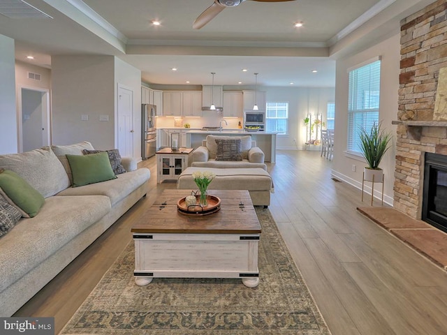 living area with wood finished floors, a ceiling fan, baseboards, a fireplace, and ornamental molding