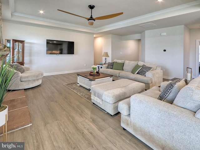 living room with a raised ceiling, wood finished floors, a ceiling fan, baseboards, and crown molding