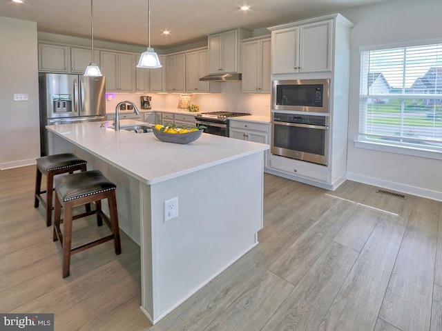kitchen featuring appliances with stainless steel finishes, a sink, light wood finished floors, a breakfast bar area, and a kitchen island with sink