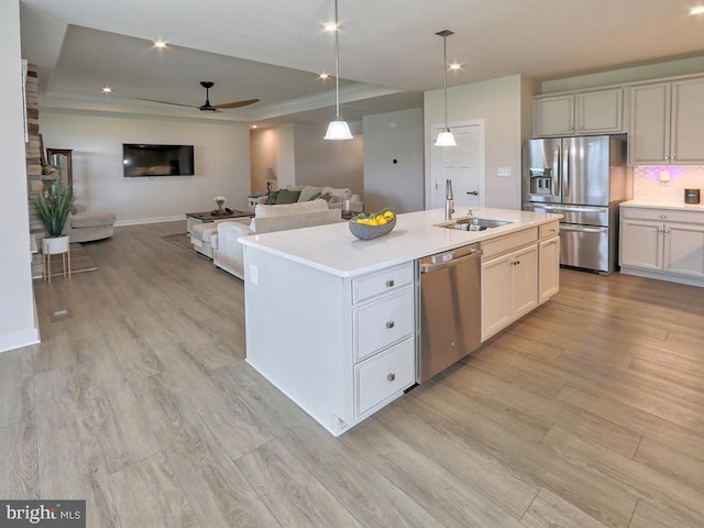kitchen featuring stainless steel appliances, a sink, a raised ceiling, light countertops, and ceiling fan