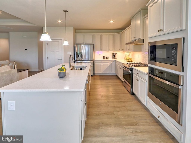 kitchen featuring stainless steel appliances, a sink, light wood finished floors, open floor plan, and a center island with sink