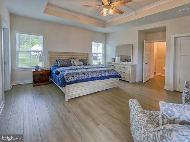 bedroom featuring baseboards, wood finished floors, crown molding, a tray ceiling, and ceiling fan