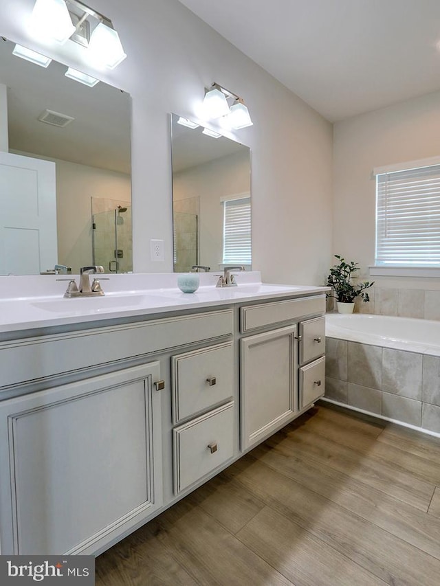 full bathroom featuring a shower stall, wood finished floors, double vanity, and a garden tub