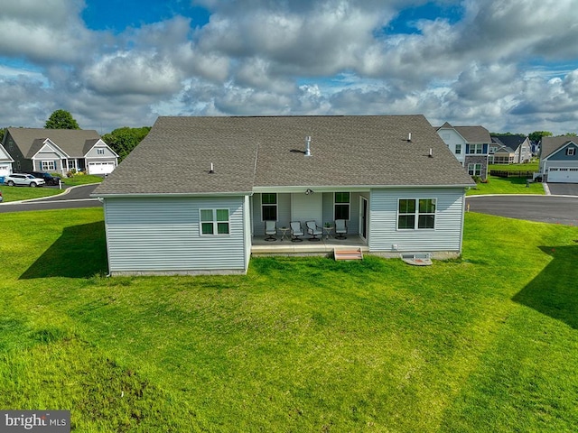 back of property featuring a patio, a yard, a residential view, and roof with shingles