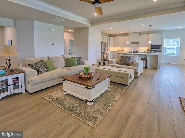 living room with light wood-style flooring, a ceiling fan, recessed lighting, and a raised ceiling