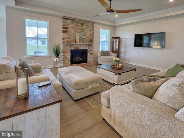 living room featuring a tray ceiling, crown molding, ceiling fan, baseboards, and wood finished floors