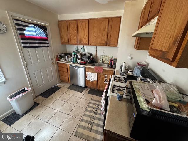 4610 6th St SE, Washington, DC 20032 - kitchen featuring stainless steel dishwasher, under cabinet range hood, brown cabinetry, light tile patterned floors, and light countertops