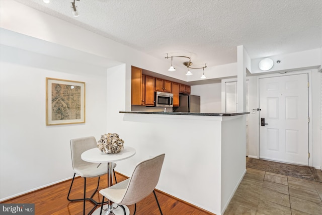 1001 N Vermont St Unit 812, Arlington, VA 22201 - kitchen featuring stainless steel microwave, brown cabinets, dark countertops, track lighting, and a textured ceiling