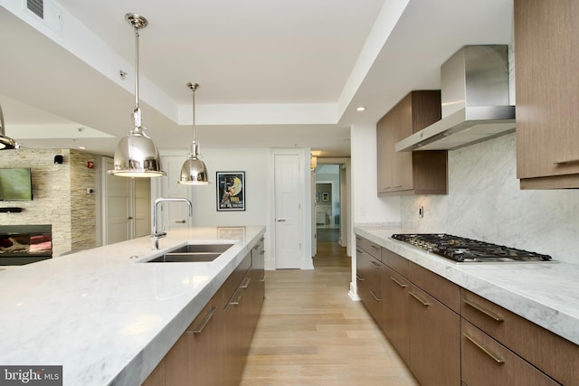 2818 Connecticut Ave NW Unit 503, Washington, DC 20008 - kitchen featuring a sink, wall chimney exhaust hood, stainless steel gas stovetop, a raised ceiling, and light wood-style floors