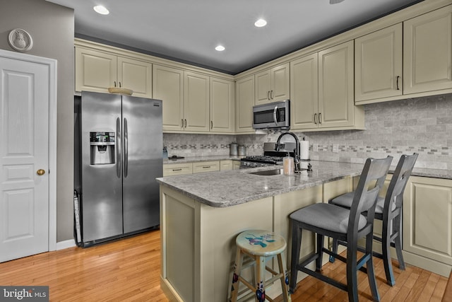 kitchen featuring stainless steel appliances, a sink, light wood-style floors, cream cabinetry, and recessed lighting