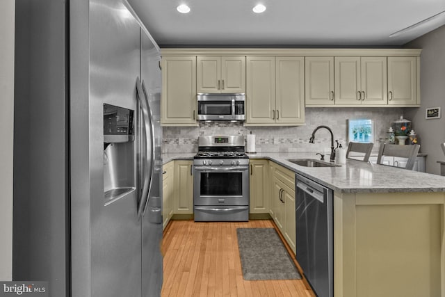 kitchen featuring stainless steel appliances, a sink, a peninsula, cream cabinetry, and light wood finished floors