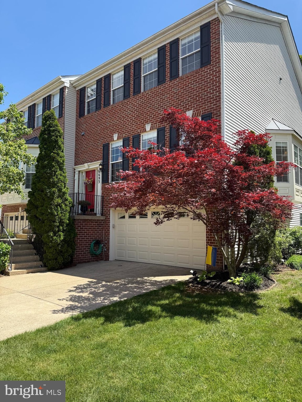 view of front of house with brick siding, an attached garage, driveway, and a front lawn