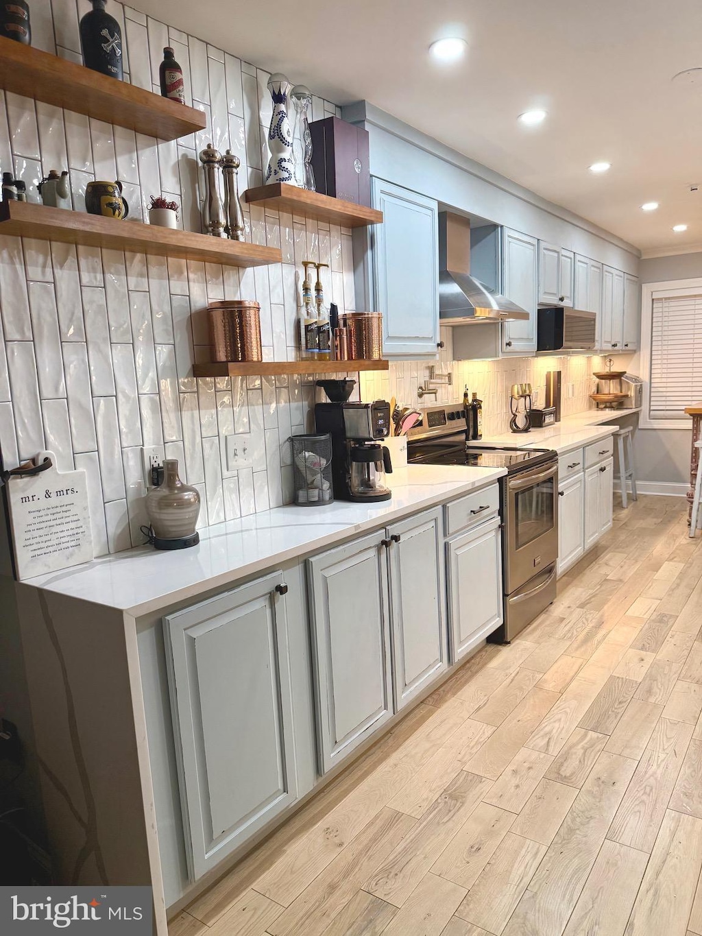 kitchen with stainless steel electric range oven, open shelves, wall chimney exhaust hood, light wood-style flooring, and backsplash