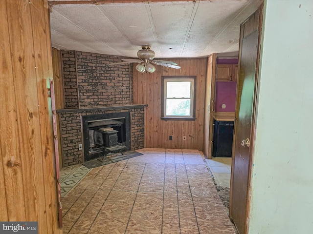 unfurnished living room with ceiling fan, wooden walls, and a wood stove