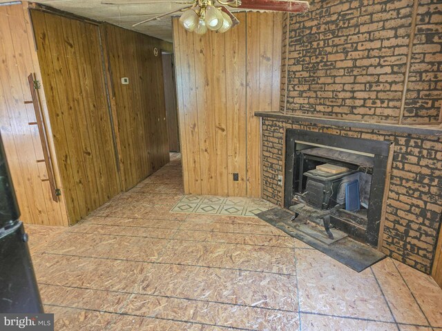 unfurnished living room featuring a wood stove, ceiling fan, and wood walls