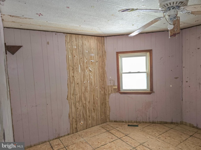 empty room featuring a ceiling fan and wood walls