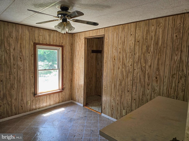 empty room featuring a ceiling fan, wood walls, and baseboards