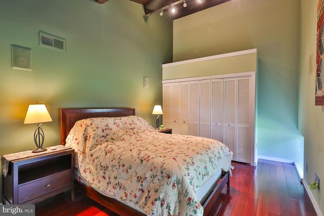 bedroom with track lighting, a closet, wood-type flooring, baseboards, and a high ceiling