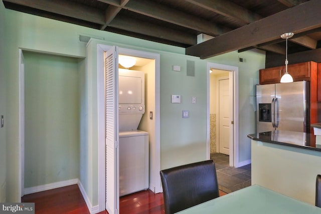 kitchen featuring stainless steel refrigerator with ice dispenser, stacked washer / dryer, beamed ceiling, brown cabinets, and pendant lighting
