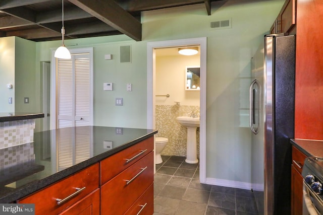 bathroom with tile patterned floors, beam ceiling, tile walls, toilet, and a wainscoted wall